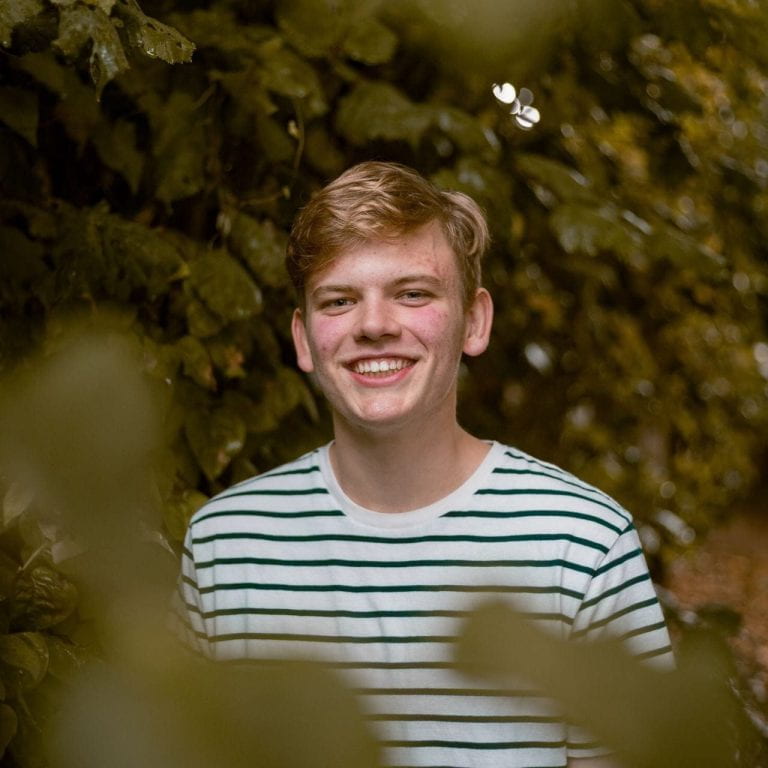 Thomas Dun peaking through leaves in a striped shirt