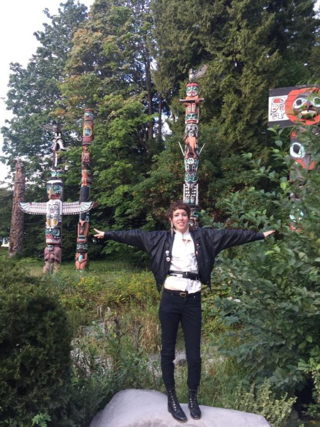 Rica Tro posing in front of a collection of totem poles